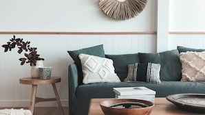 Un salón acogedor con un sofá verde oscuro, una mesa de centro de madera y una mesita auxiliar redonda con una planta.
