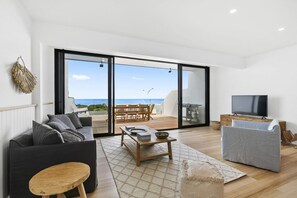 Una sala de estar moderna con sofá, mesa de centro y televisor, que da a un balcón con vista al mar.
