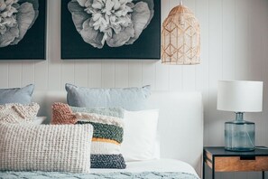 Ein ordentlich eingerichtetes Schlafzimmer mit einem Bett, Kissen, einem Nachttisch mit Lampe und zwei an der Wand hängenden Blumenbildern.