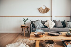 Ein gemütliches Wohnzimmer mit einer grauen Couch, gemusterten Kissen, einem Holz-Couchtisch und einer gewebten Wanddeko.