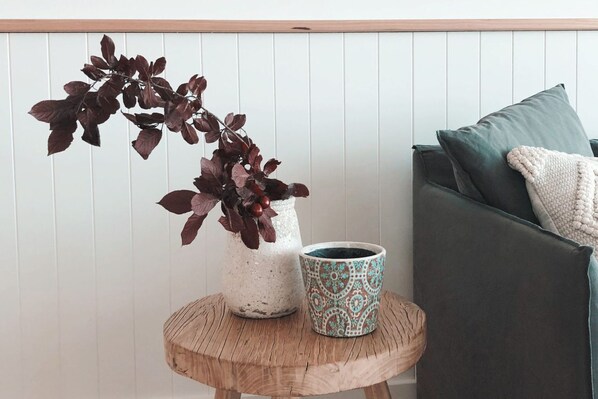 Eine Pflanze in einem weißen Topf und eine gemusterte Tasse auf einem Holztisch neben einem dunklen Sofa mit Kissen.