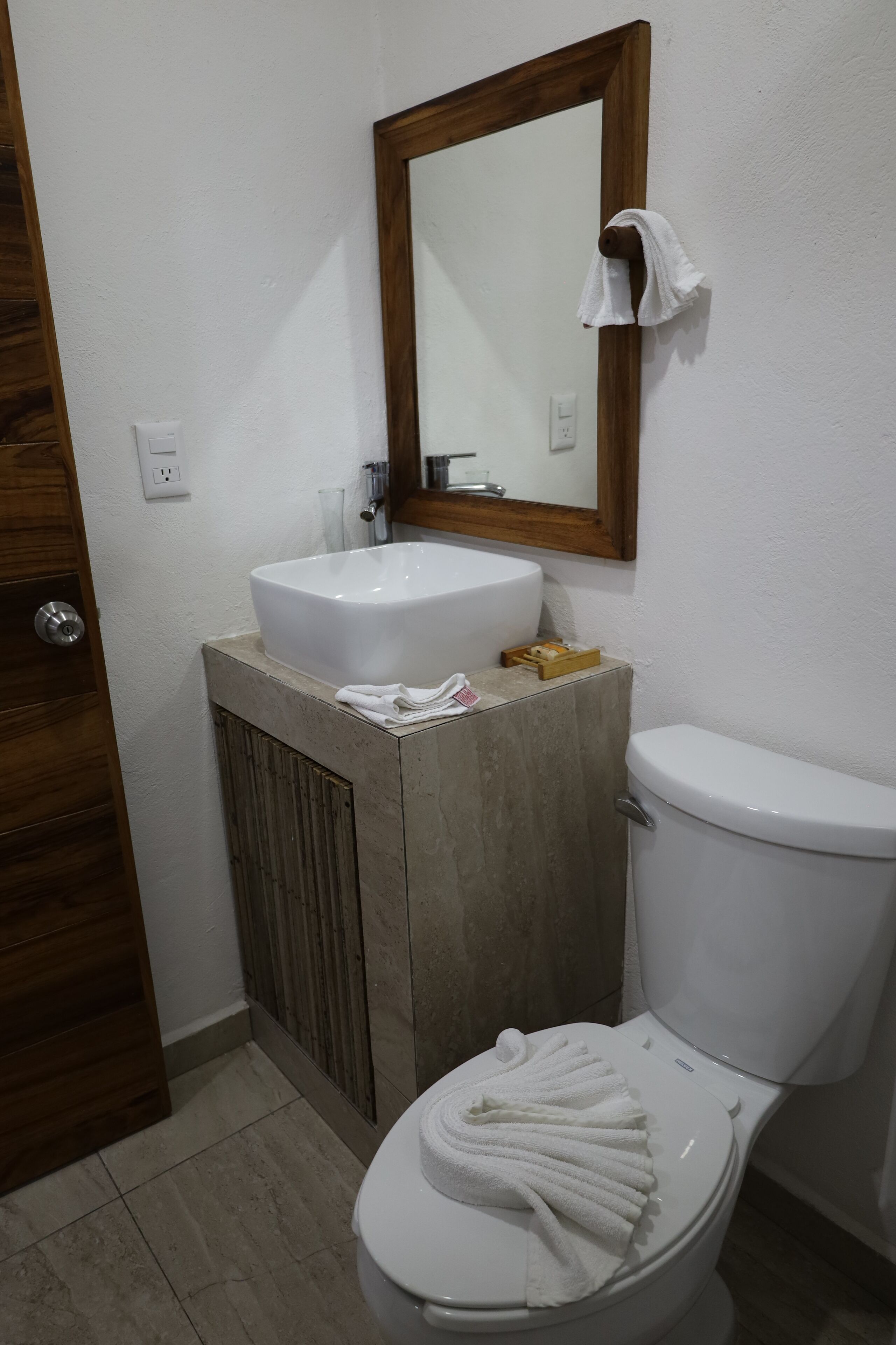 Un baño con lavamanos blanco, mueble de madera y un inodoro con una toalla.