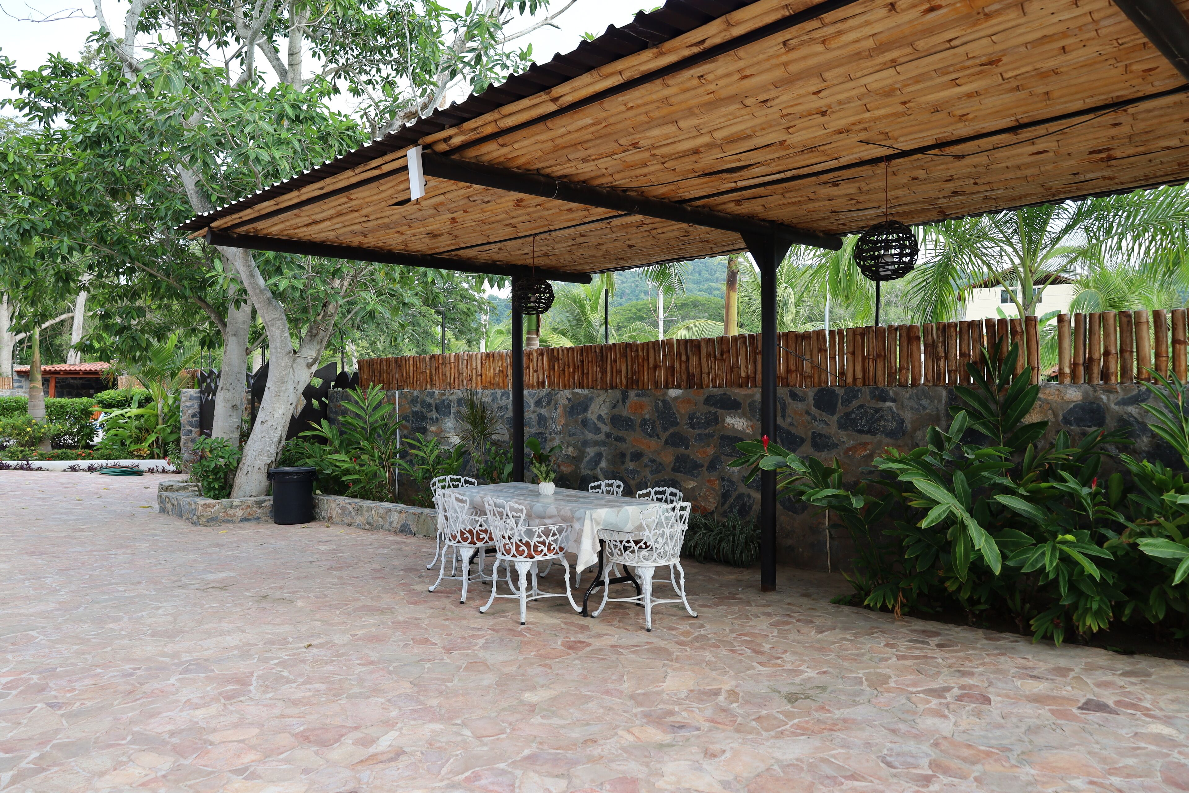 An outdoor patio with stone flooring, white metal chairs, and a table.