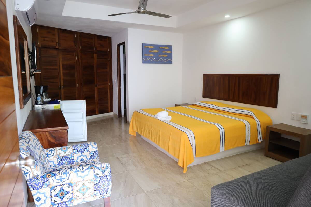 Una habitación de hotel con cama, escritorio, silla, armario y ventilador de techo.