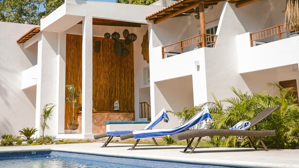 Un complexe hôtelier moderne doté d’une piscine, de chaises longues et d’une porte en bois.