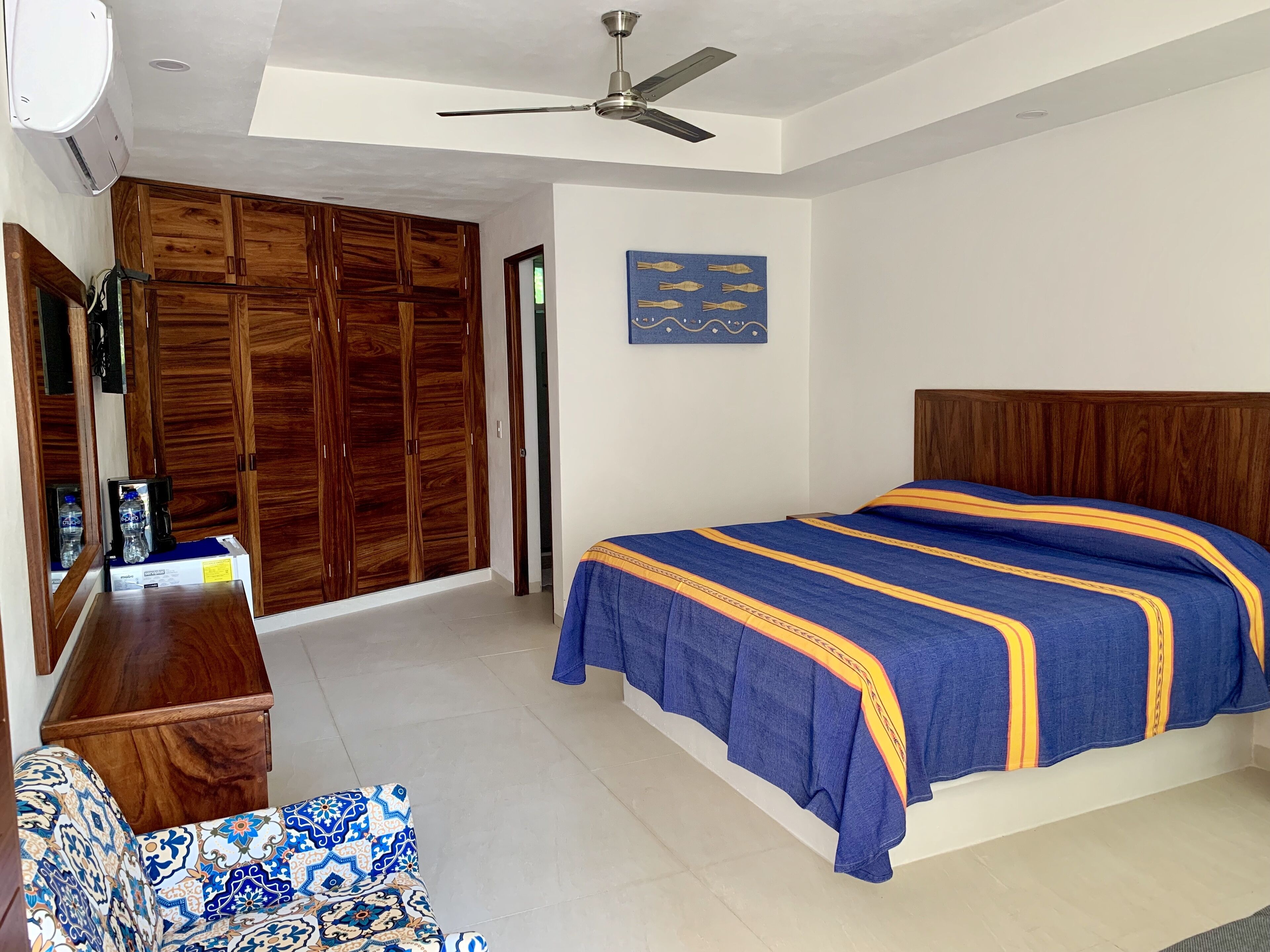 A bedroom with a bed, wooden wardrobe, ceiling fan, and a wall with a fish pattern.