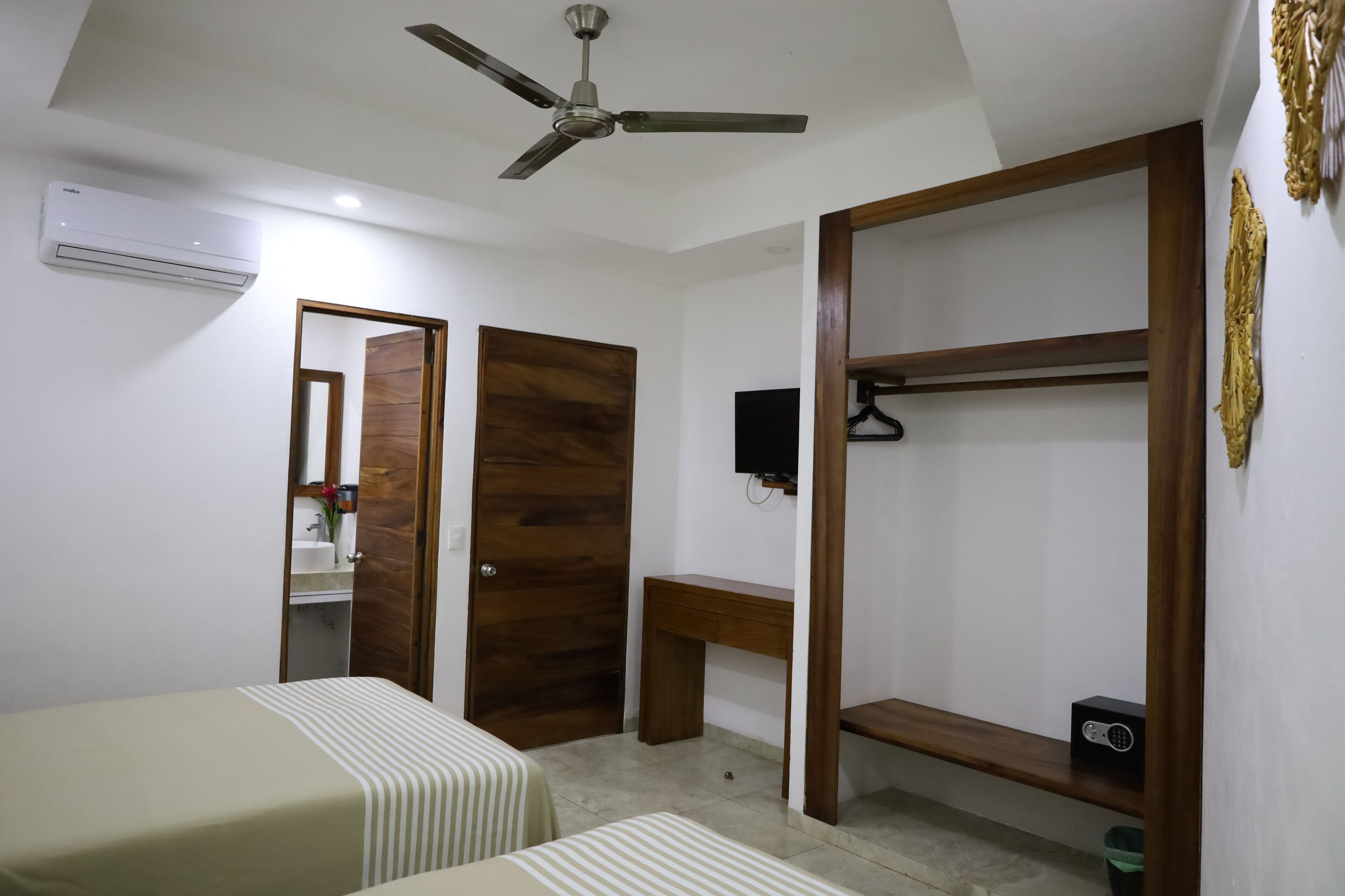 Un dormitorio con una cama, un armario de madera, un escritorio, un ventilador de techo y un televisor.