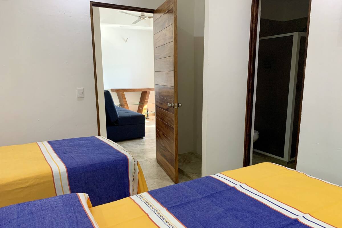 Una habitación con dos camas, un armario de madera, una silla y una puerta que da a otra estancia.