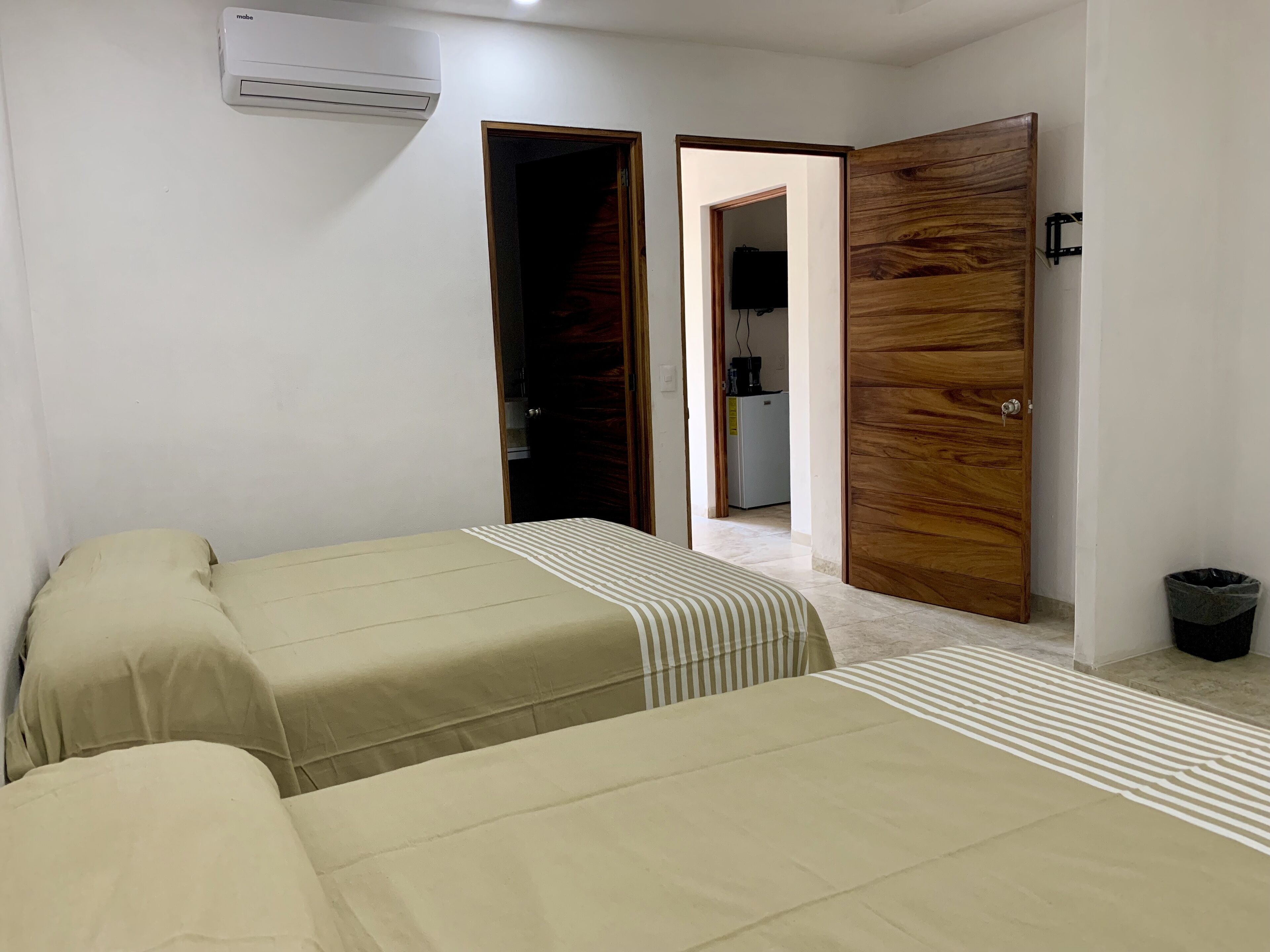 A bedroom with two beds, a wooden wardrobe, an air conditioning unit, and a trash bin.