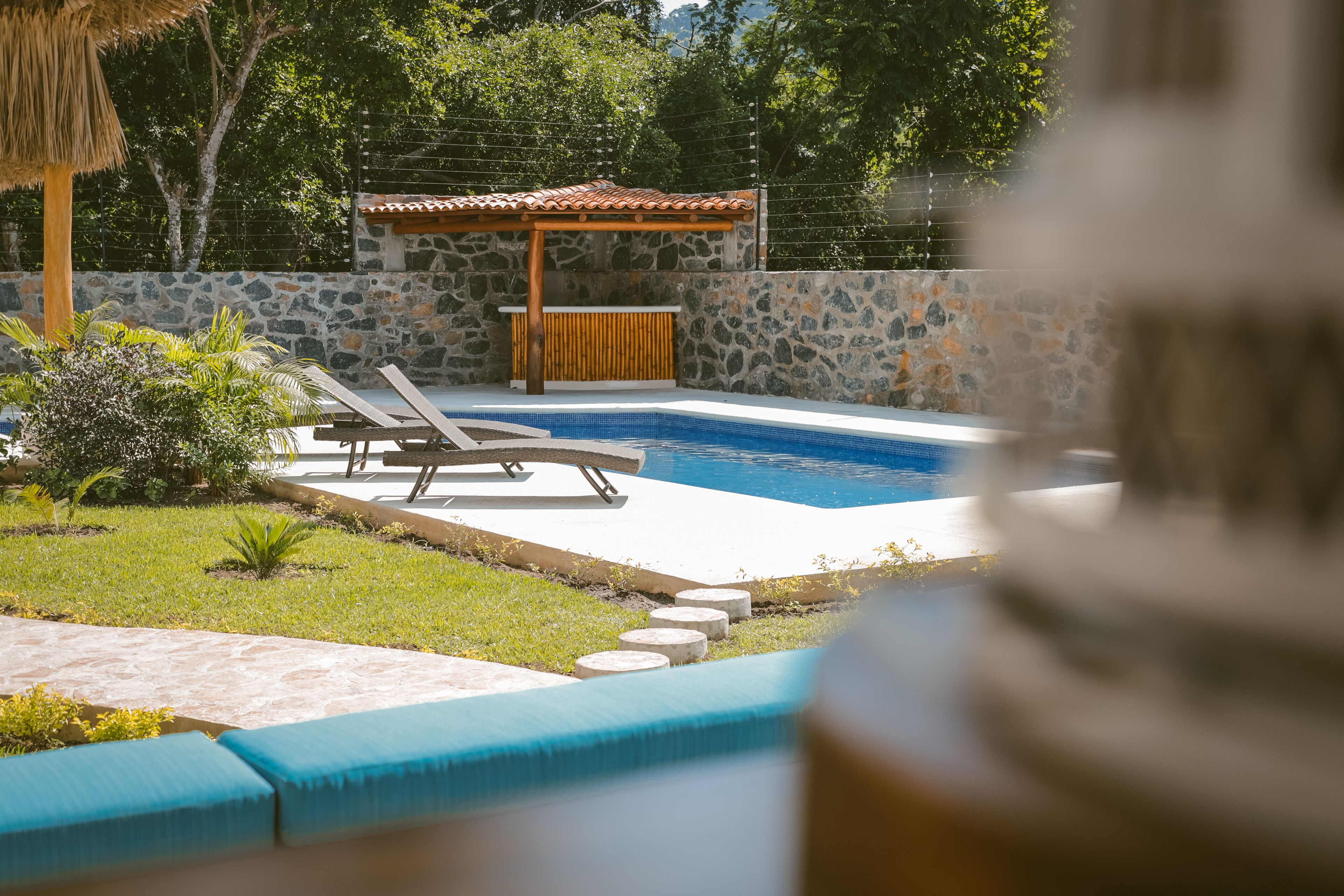 Une piscine avec des chaises longues, un mur en pierre et une pergola en bois.