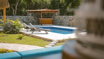 Une piscine avec des chaises longues, un mur en pierre et une pergola en bois.