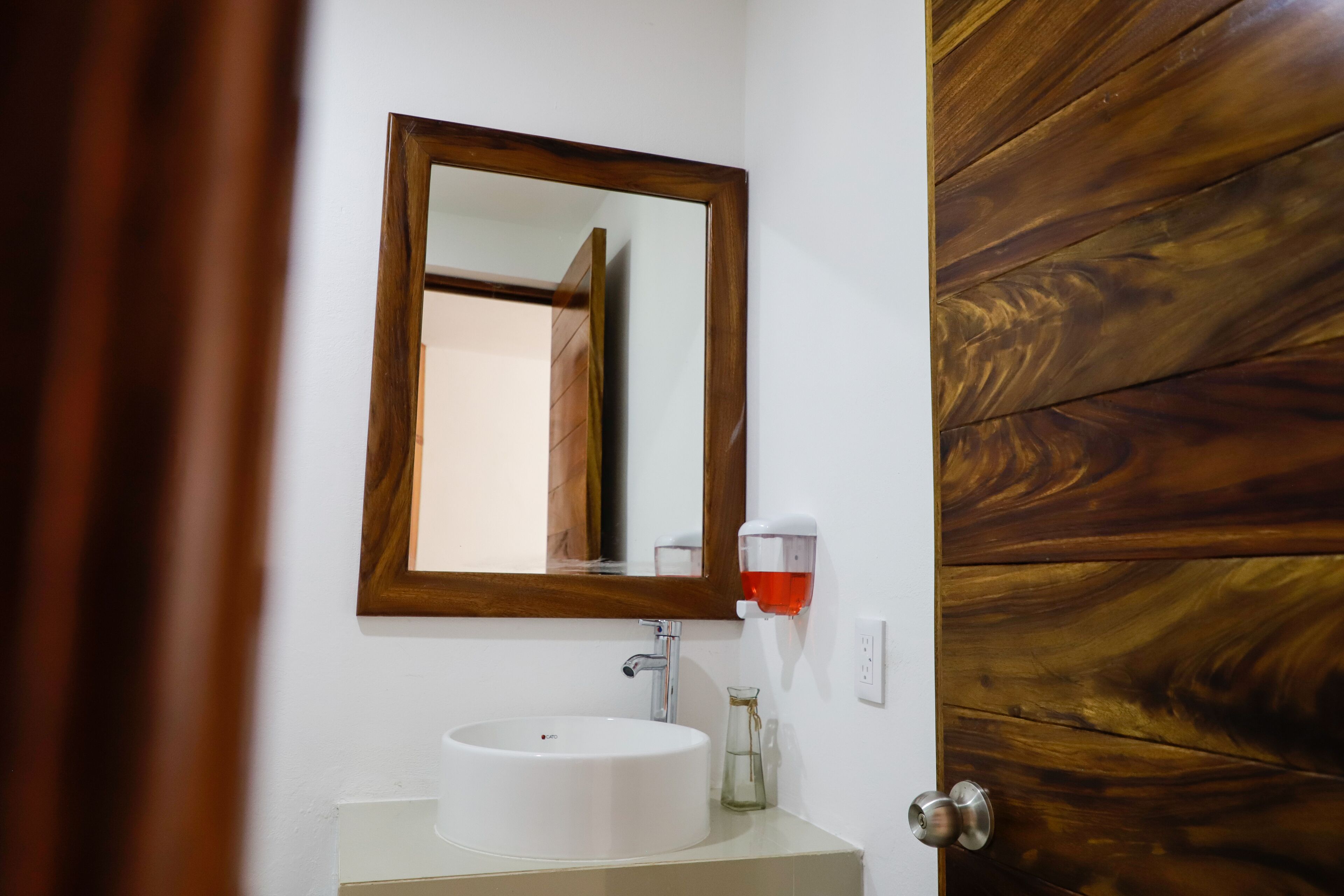 Ein Badezimmer mit einem weißen Waschbecken, einer Holztür und einem Spiegel mit Holzrahmen.
