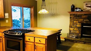 Una cocina con armarios de madera, horno empotrado, estufa a gas, chimenea de piedra y un ventanal grande.