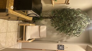 Une pièce avec un bureau en bois, un téléviseur, une plante en pot et un panneau accroché au mur.
