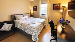 Une chambre d’hôtel équipée d’un lit, d’un bureau, d’une chaise, d’un ventilateur de plafond, d’une fenêtre avec des rideaux et d’un téléviseur fixé au mur.