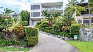 A modern building with a landscaped driveway and a stone wall. - Luxury 4 bedroom, 4 bathroom apartment in Central Airlie with the best views (Airlie Beach)