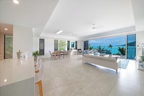 A spacious living area with a large window overlooking a scenic view, a dining area with a table and chairs, and a modern kitchen with a white countertop.