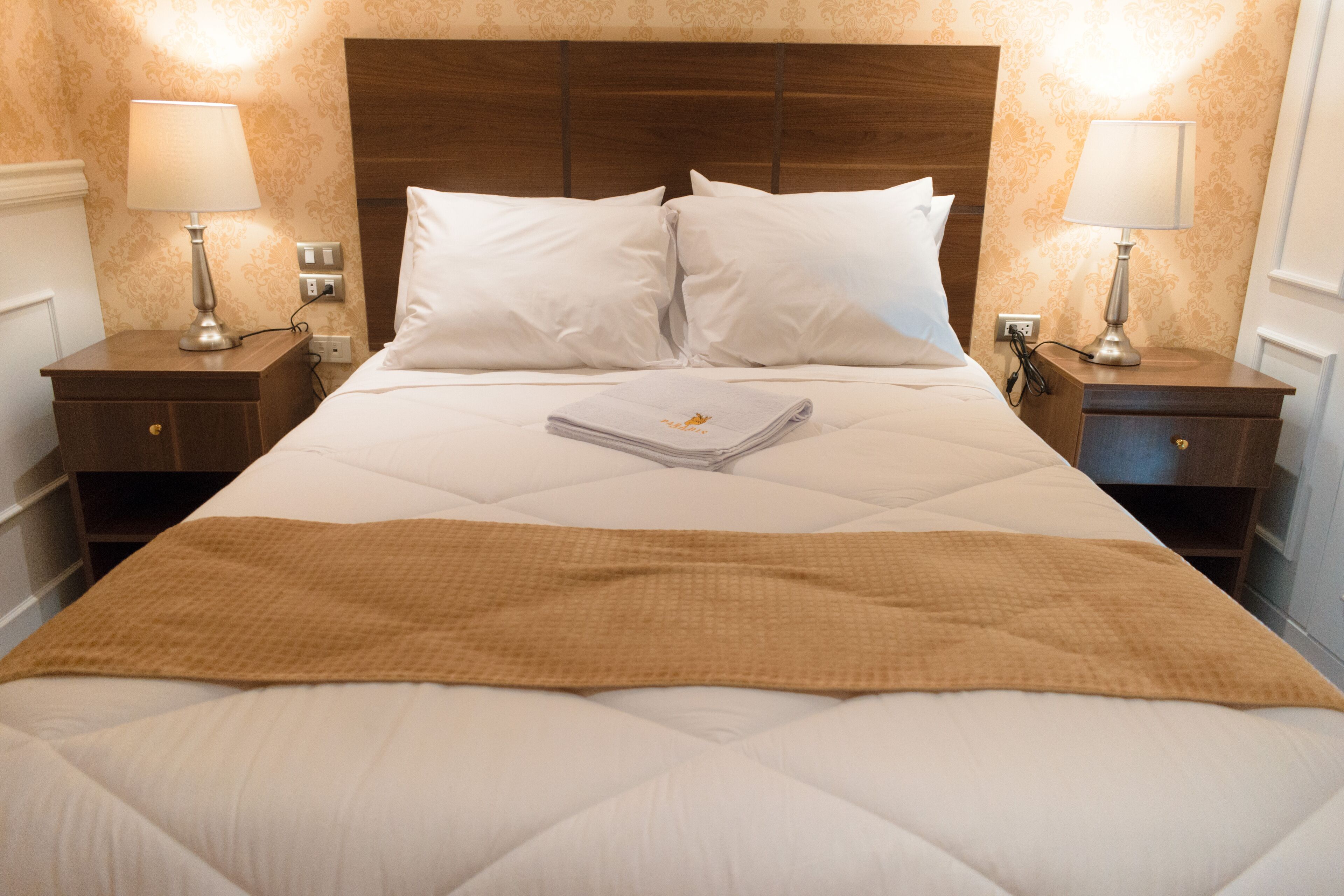 A neatly made bed with white linens, a brown throw blanket, and two bedside lamps on wooden nightstands.