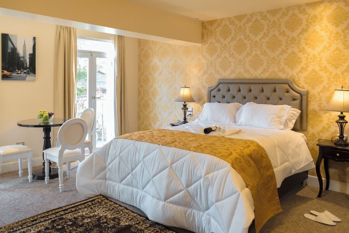 Ein Hotelzimmer mit einem großen Bett, zwei Nachttischlampen, einem kleinen Tisch mit einem Sessel und einem Stadtbild.