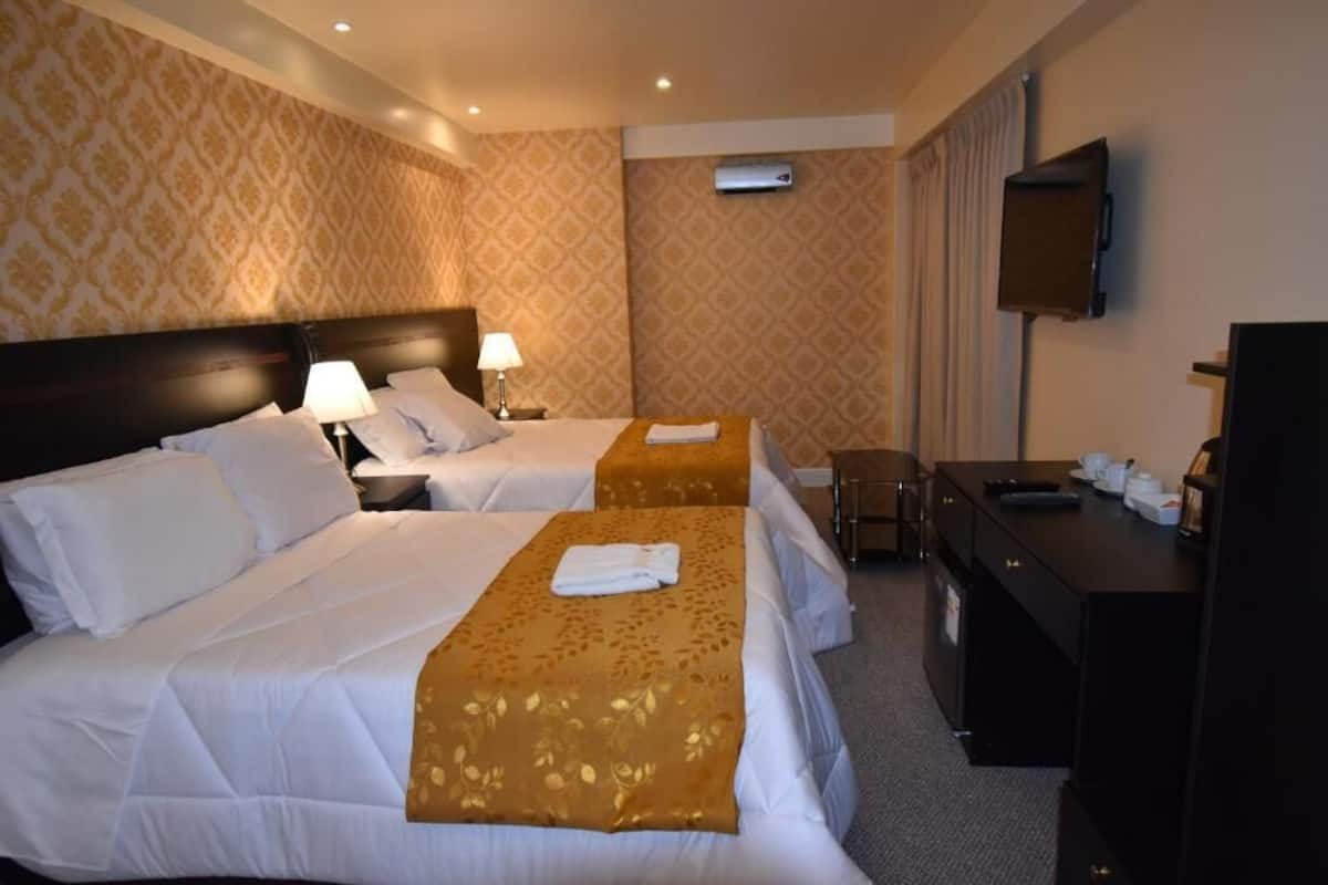 Ein Hotelzimmer mit zwei Betten, einem Schreibtisch, einem Sessel, einem Fernseher und einer Wand-Klimaanlage.