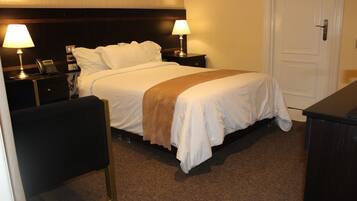 Quarto de hotel com uma cama, duas mesas de cabeceira com abajures, um telefone e uma porta.