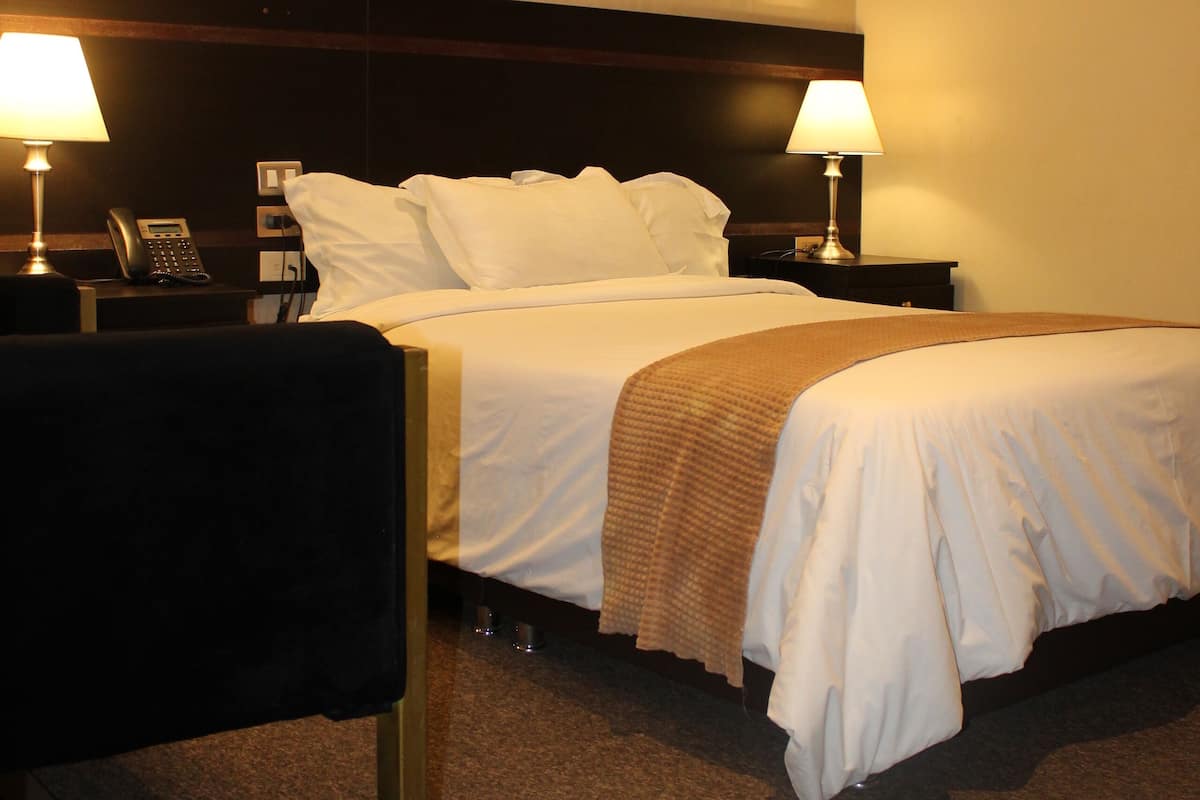 Ein Hotelzimmer mit einem großen Bett, zwei Nachttischen mit Lampen, einem Telefon und Teppichboden.