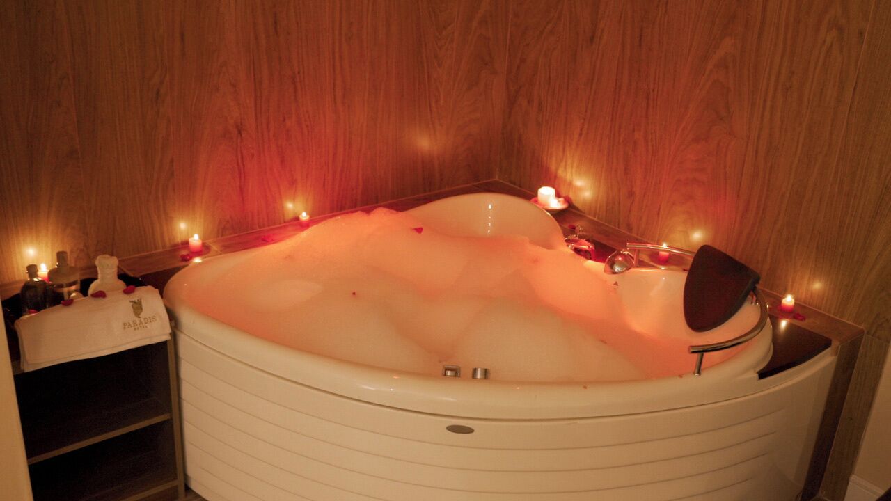 A hot tub with bubbles, surrounded by candles and bottles, in a wooden room.