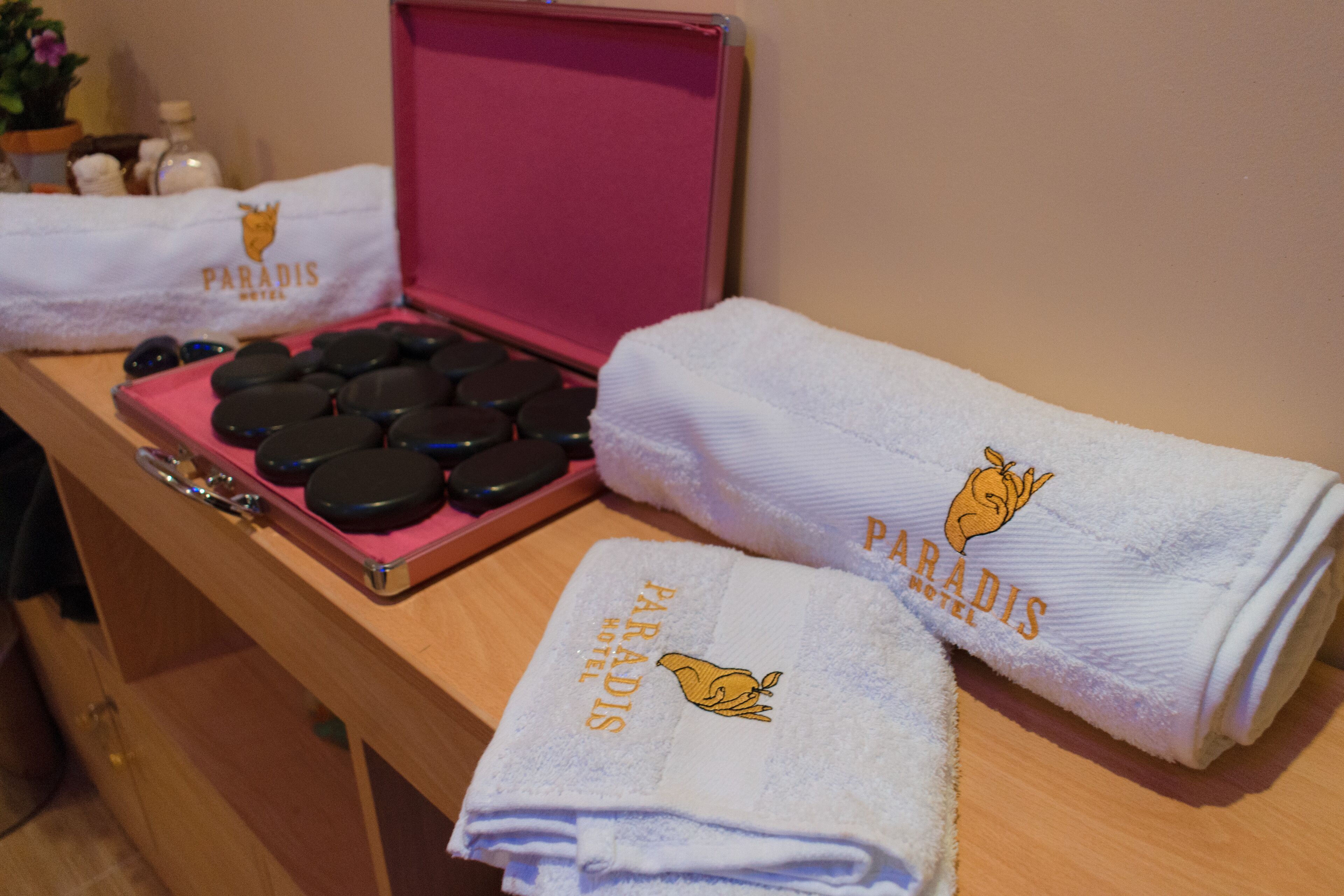 Una encimera de baño con un juego de piedras de masaje negras, una pistola de masaje rosa y dos toallas con el logotipo del Paradise Hotel.