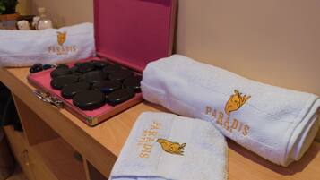 Una encimera de baño con un juego de piedras de masaje negras, una pistola de masaje rosa y dos toallas con el logotipo del Paradise Hotel.