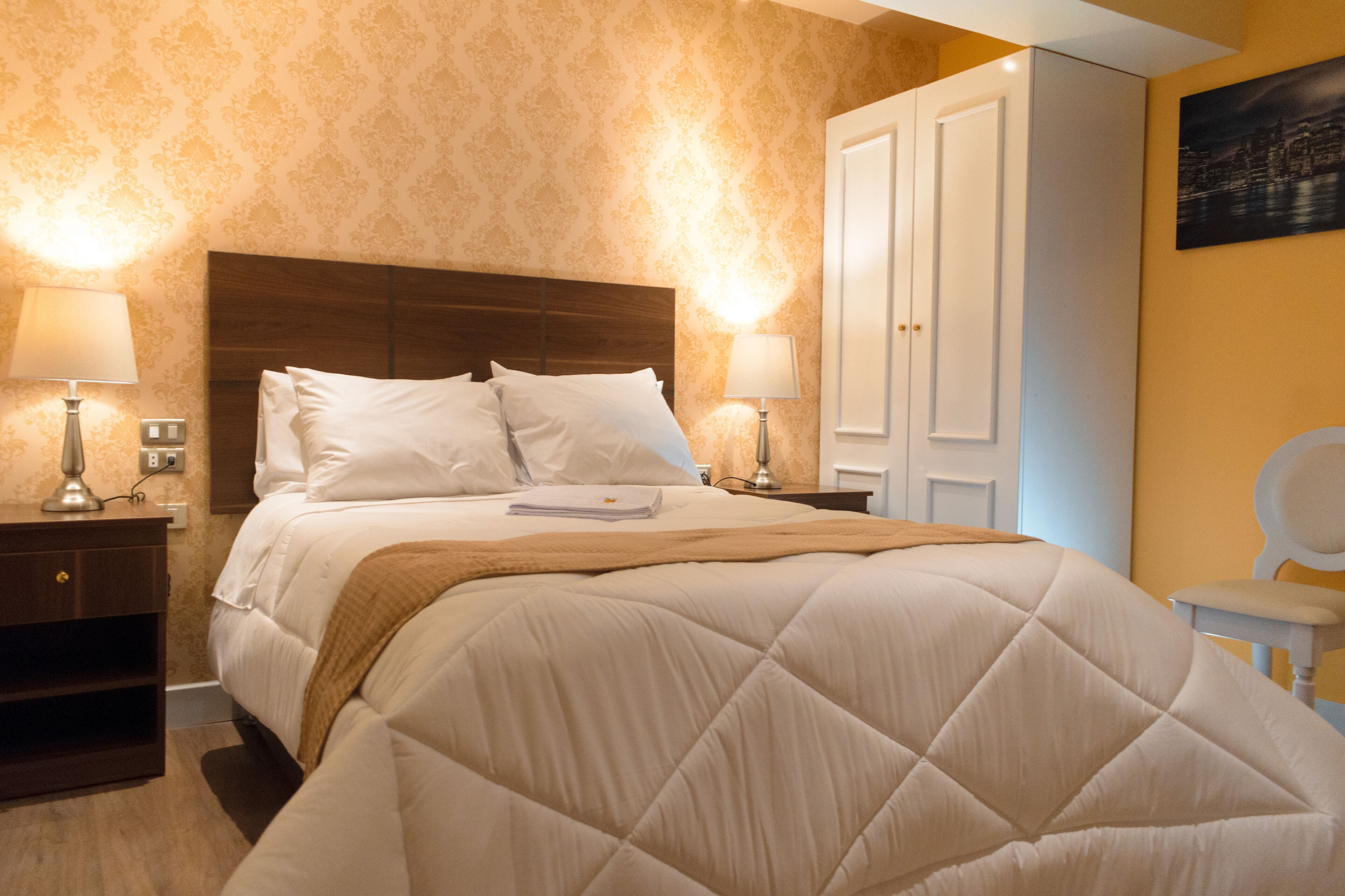 Cama bem arrumada com cabeceira acolchoada, duas luminárias de cabeceira e mesa de apoio com abajur.