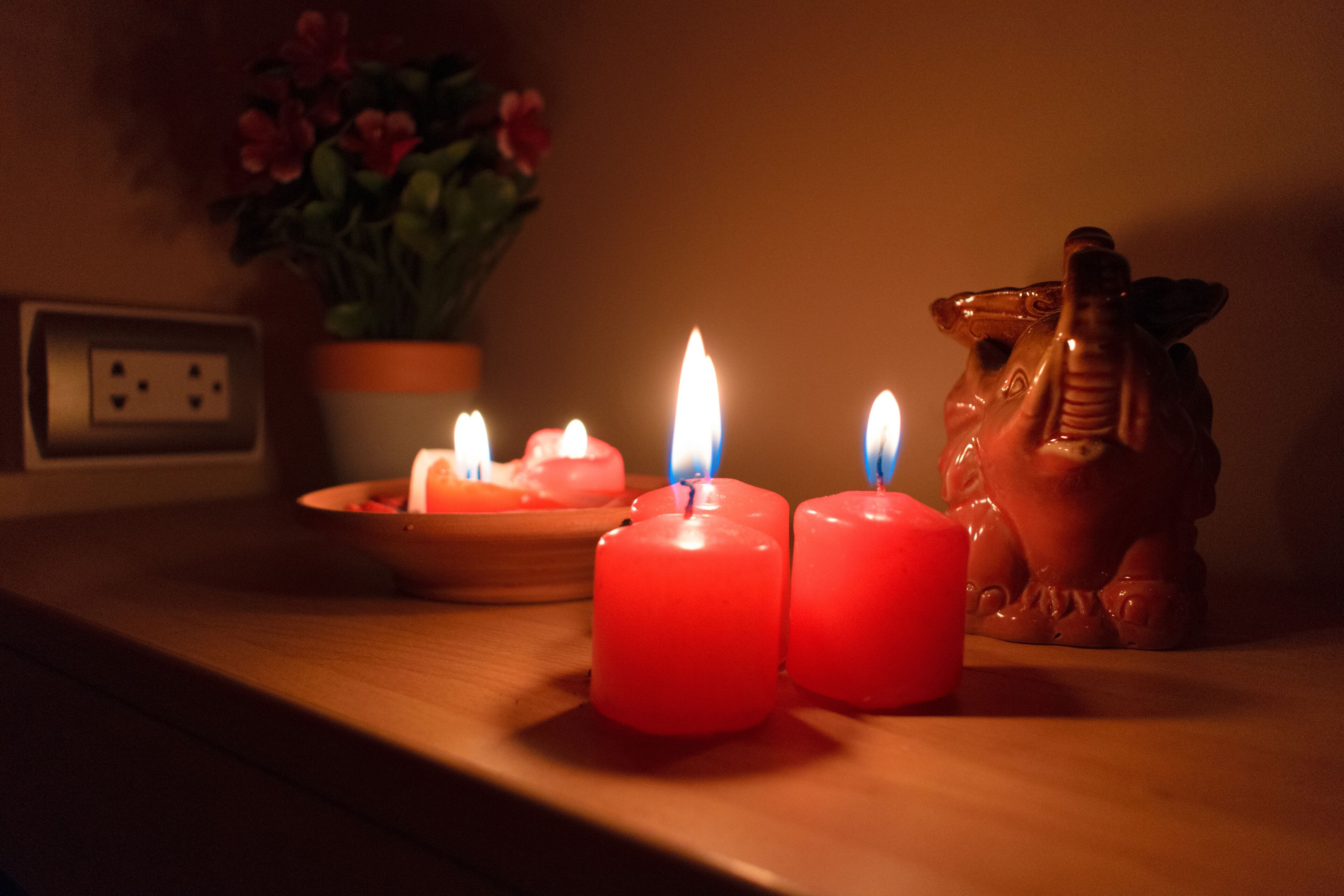 Tres velas encendidas sobre una superficie de madera, una planta pequeña al fondo y una figurita de cerámica.