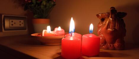 Tres velas encendidas sobre una superficie de madera, una planta pequeña al fondo y una figurita de cerámica.