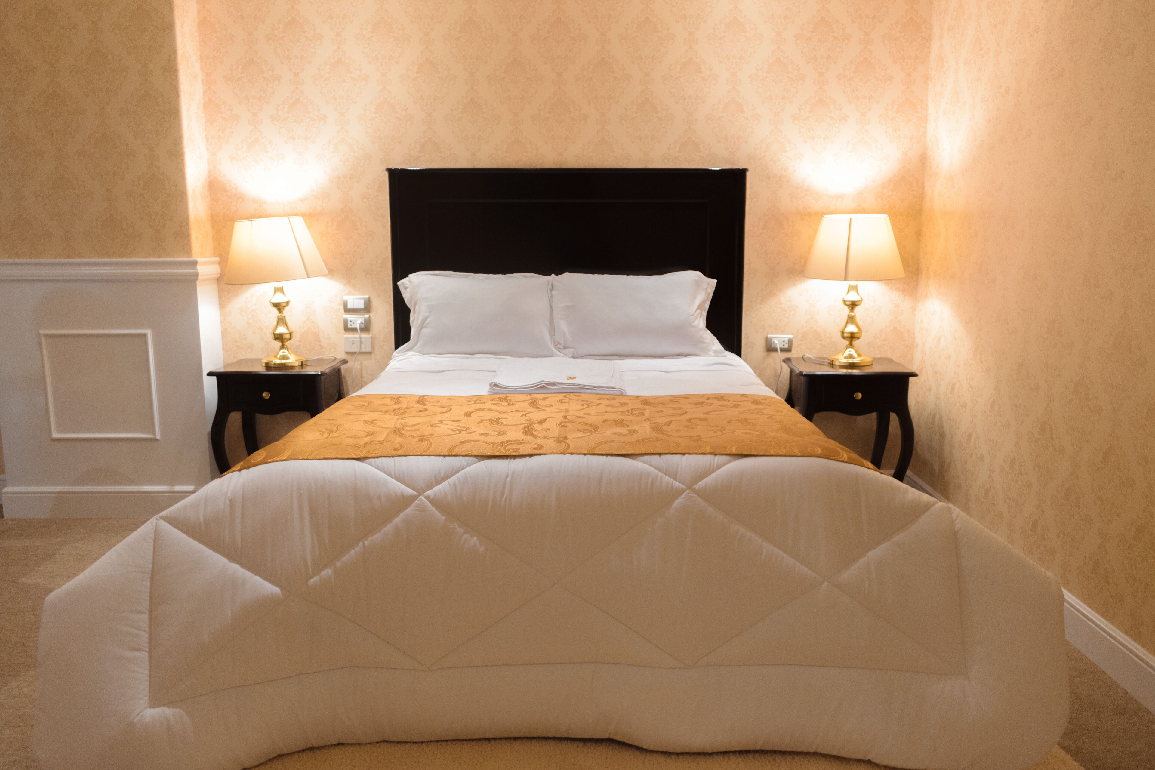 Una cama bien hecha con un cabecero acolchado, dos mesitas de noche con lámparas y un suelo cubierto de alfombra.