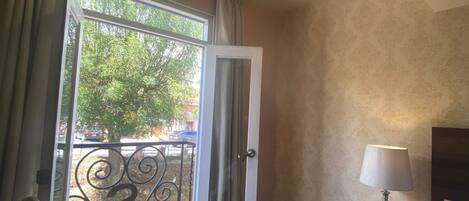 A hotel room with a wooden floor, a desk with a lamp, a telephone, and a view of the outdoors through a glass door.