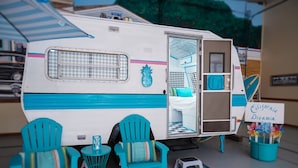 A travel trailer with a kitchen area, two turquoise chairs, a small table, and a sign reading "California Dreamin'". - Lone Star Glamp Inn (Round Top)