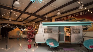 A vintage trailer with a turquoise awning, a red potted plant, and two turquoise chairs. - Lone Star Glamp Inn (Round Top)