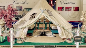 A tented display area with a vintage Cadillac sign, a cowhide rug, and a 'Squash Blossom' sign. - Lone Star Glamp Inn (Round Top)