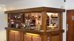 A bar area with a brick wall and wooden counter, featuring various bottles and glasses.