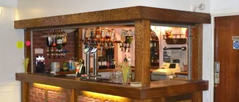 A bar area with a brick wall and wooden counter, featuring various bottles and glasses.