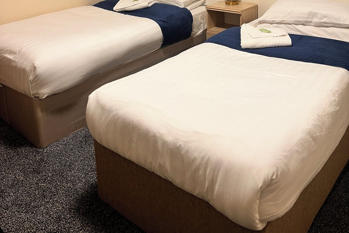 A hotel room with two beds, a wall-mounted artwork of hearts, and a bedside table with a lamp.