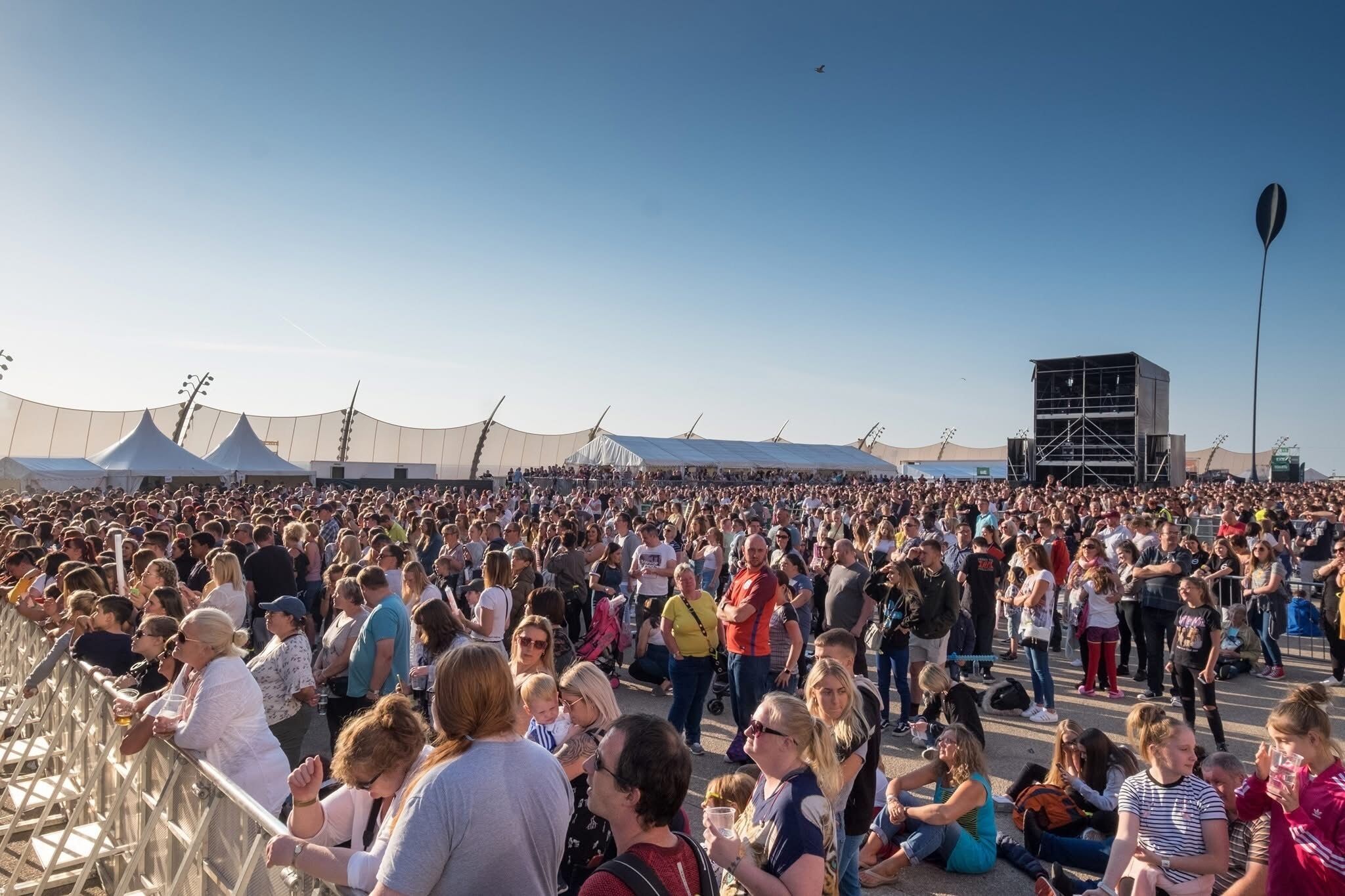 A large outdoor gathering with a stage and tents in the background.