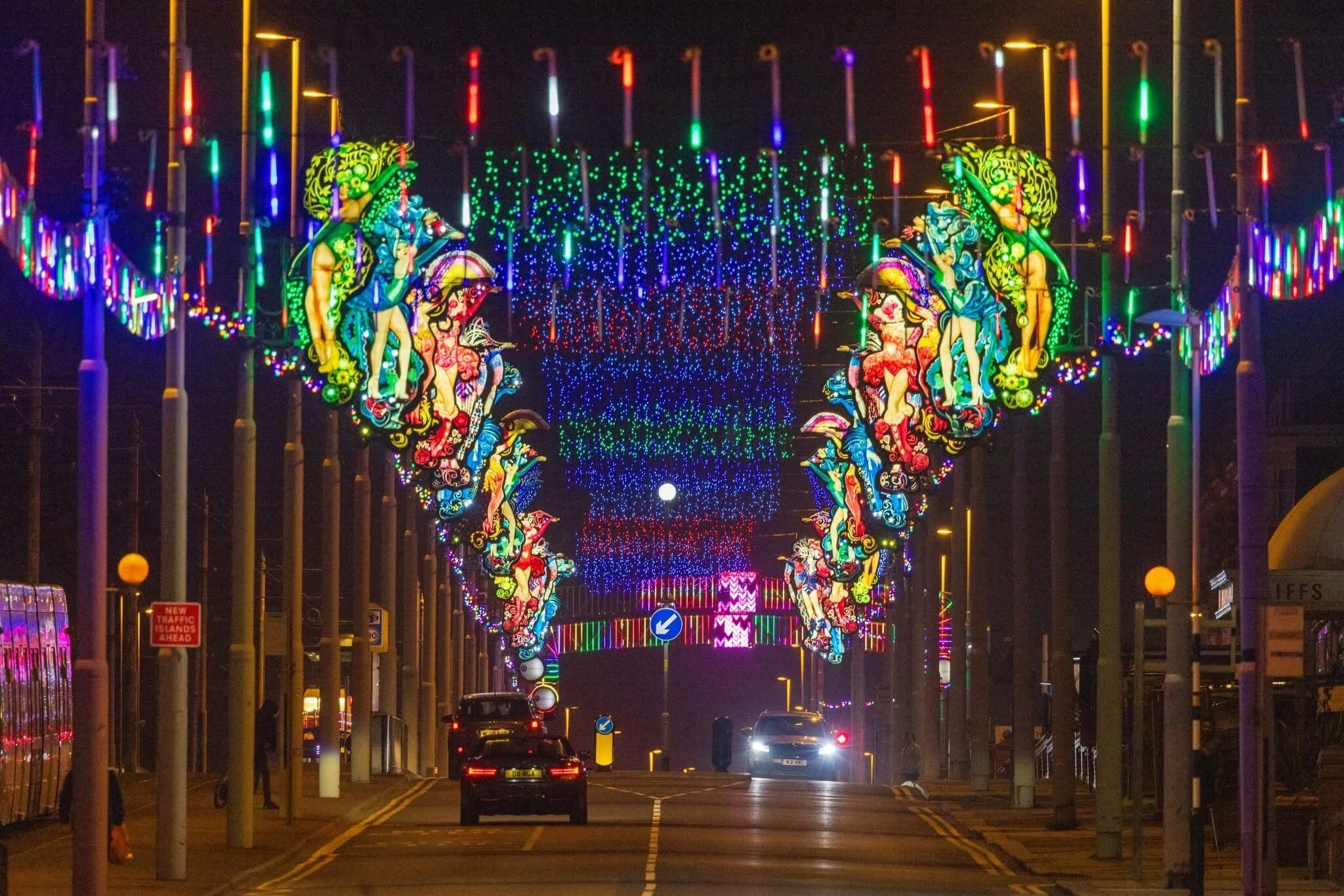 A street with colorful lights and decorations, including two large figures on either side of the road.