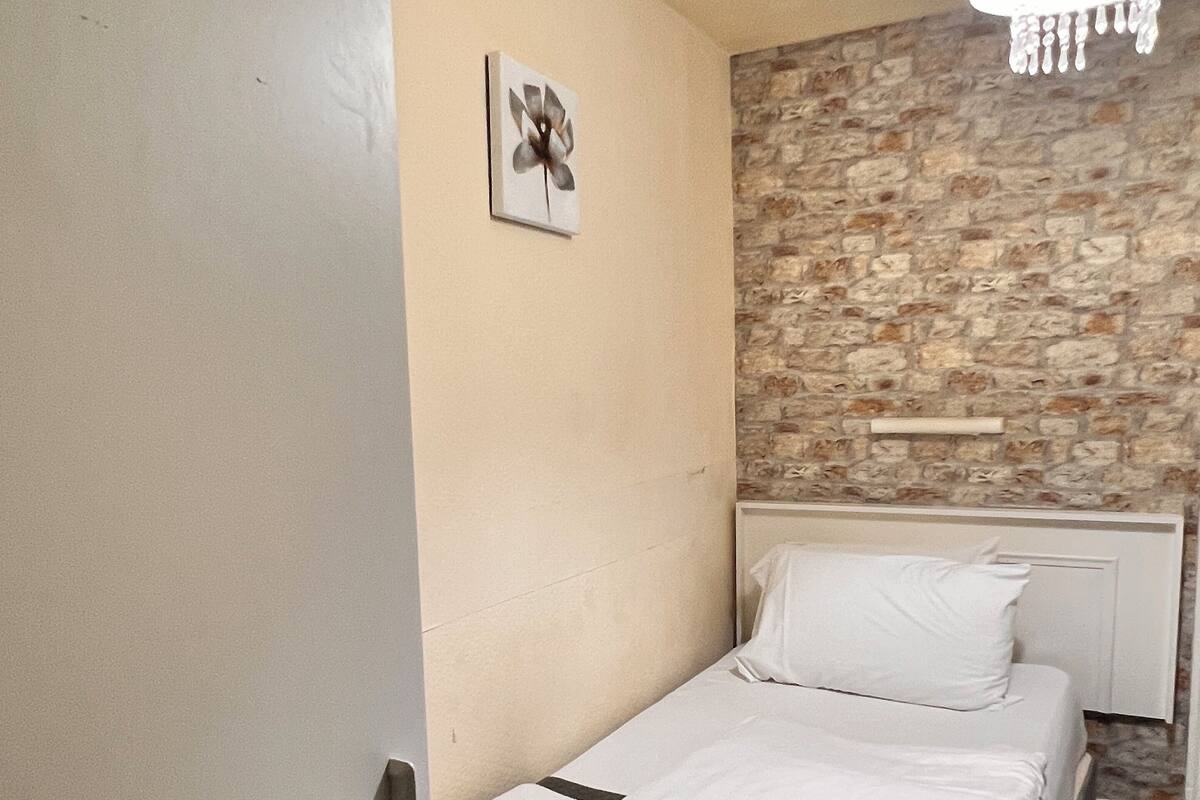 A small, single-bed room with a stone wall and a white ceiling.