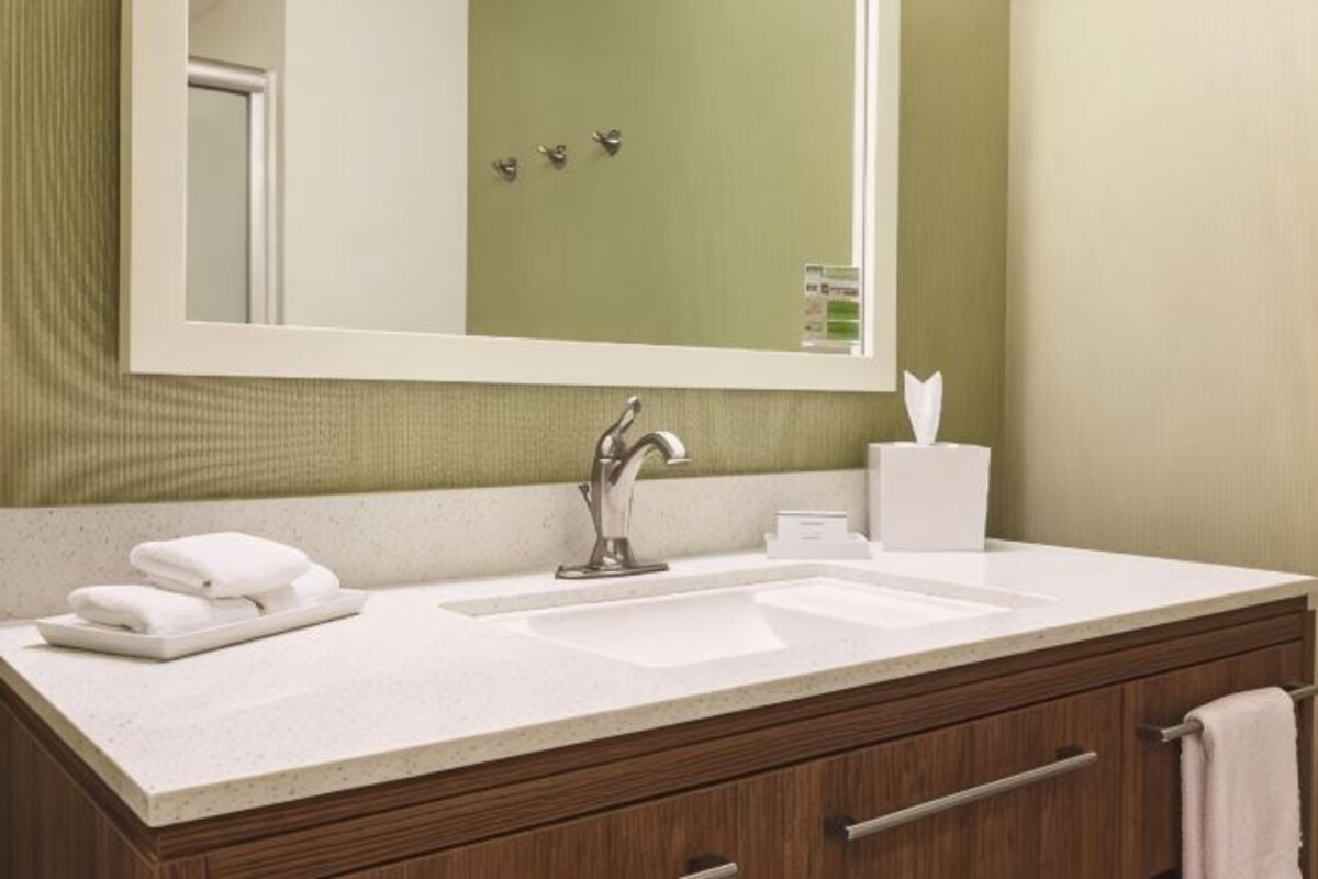 A bathroom with a sink, mirror, towel rack, and a tissue box.