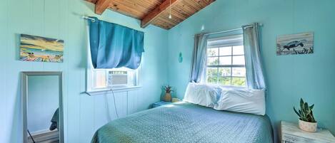 A bedroom with a bed, a window with curtains, a ceiling fan, and a small table with a plant.