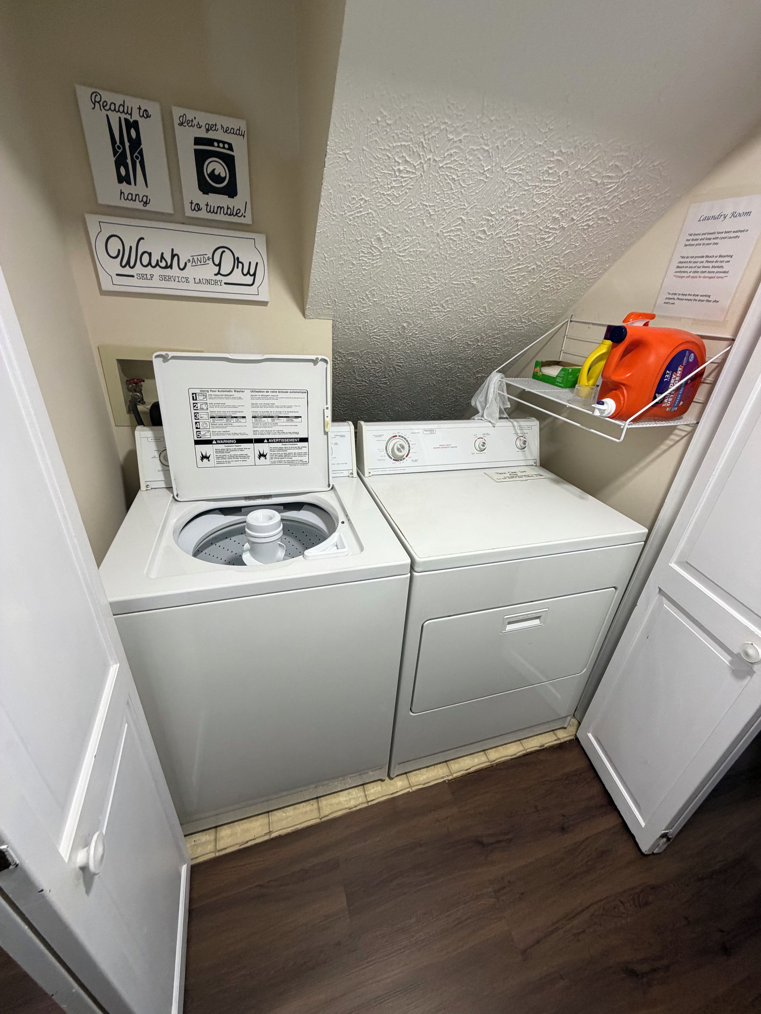 A compact laundry room with a front-loading washing machine, a dryer, and a shelf with cleaning supplies.