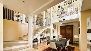 Amplia sala de estar con escalera que conduce a un balcón, comedor con mesa para cuatro y un gran armario de madera.
