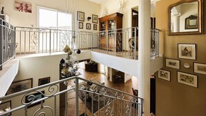 Un interior espacioso con techo alto, un balcón con barandilla ornamentada y una escalera que conduce a un nivel superior.