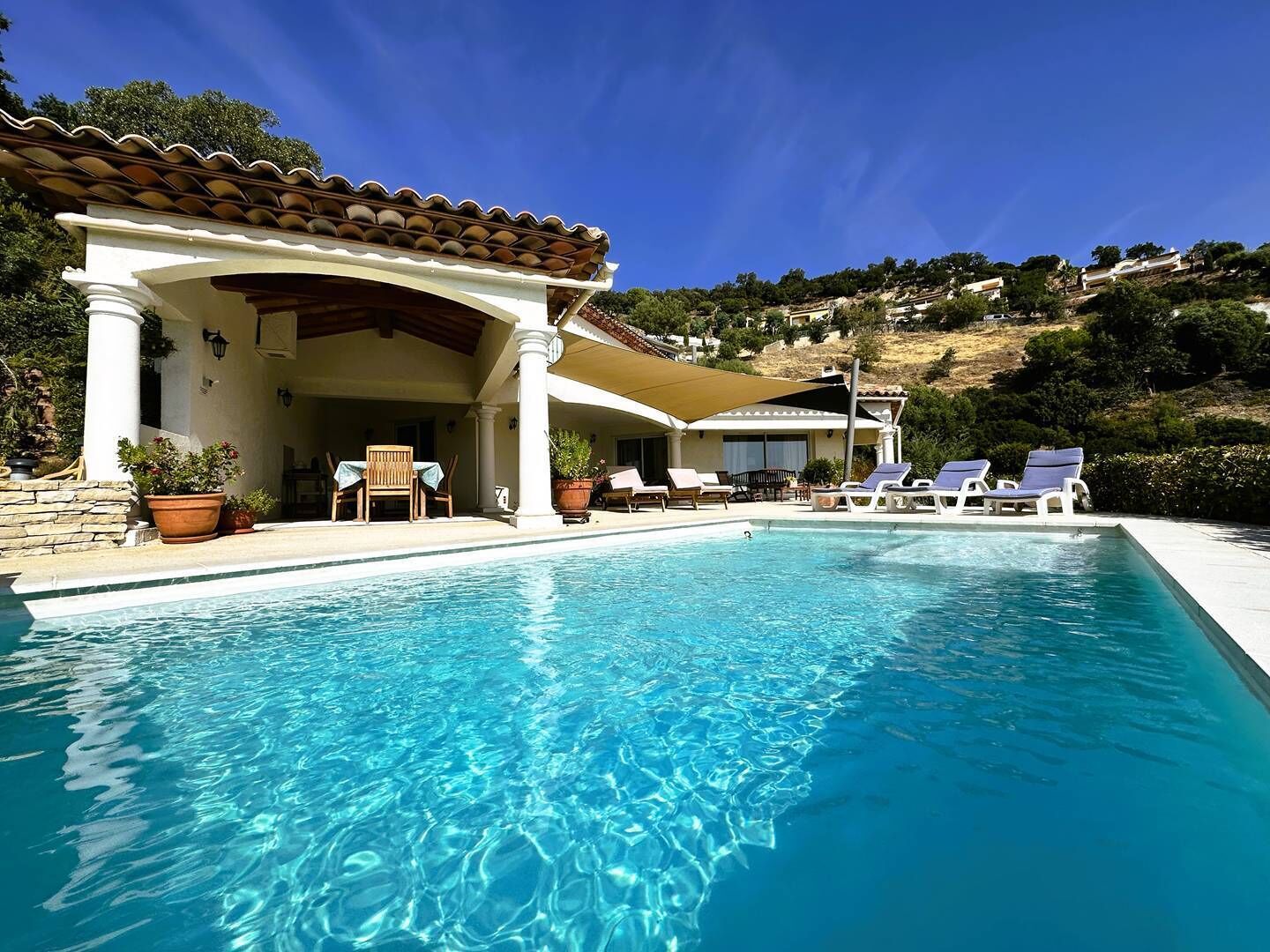 A pool area with lounge chairs, a covered seating area, and a view of a hillside.
