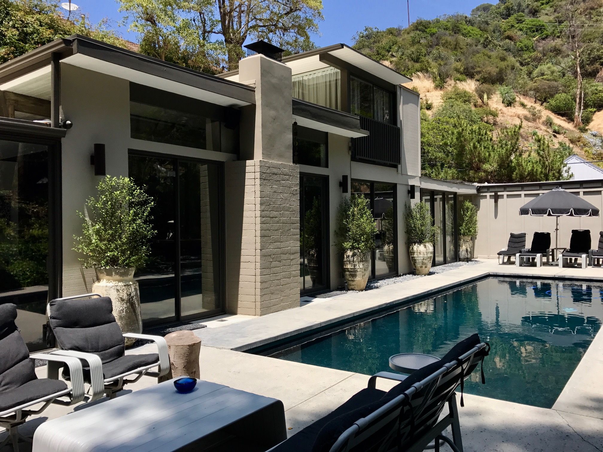 Ein modernes Haus mit Schwimmbad, Außenbereich zum Sitzen und einer Hanglage im Hintergrund.